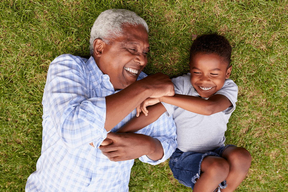 Grandfather lying on grass with grandchild laughing together