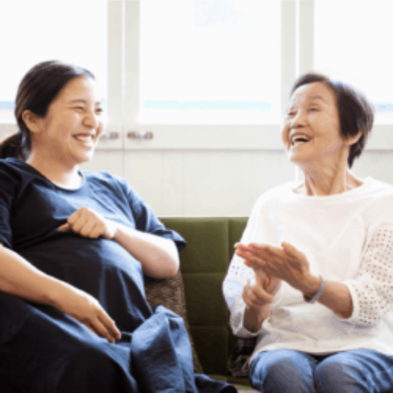 Pregnant woman sitting on a couch with an older woman laughing